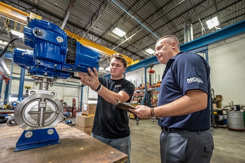 two mce employees working on a blue and silver heavy machinery tool